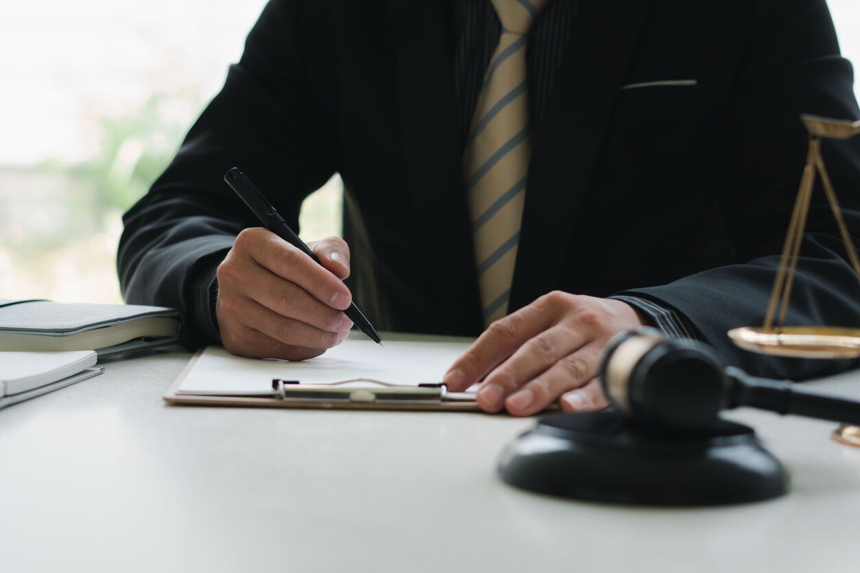 Criminal defense lawyer writing on a legal document, with a gavel and scales of justice on the desk, symbolizing diligent legal representation in Albany.