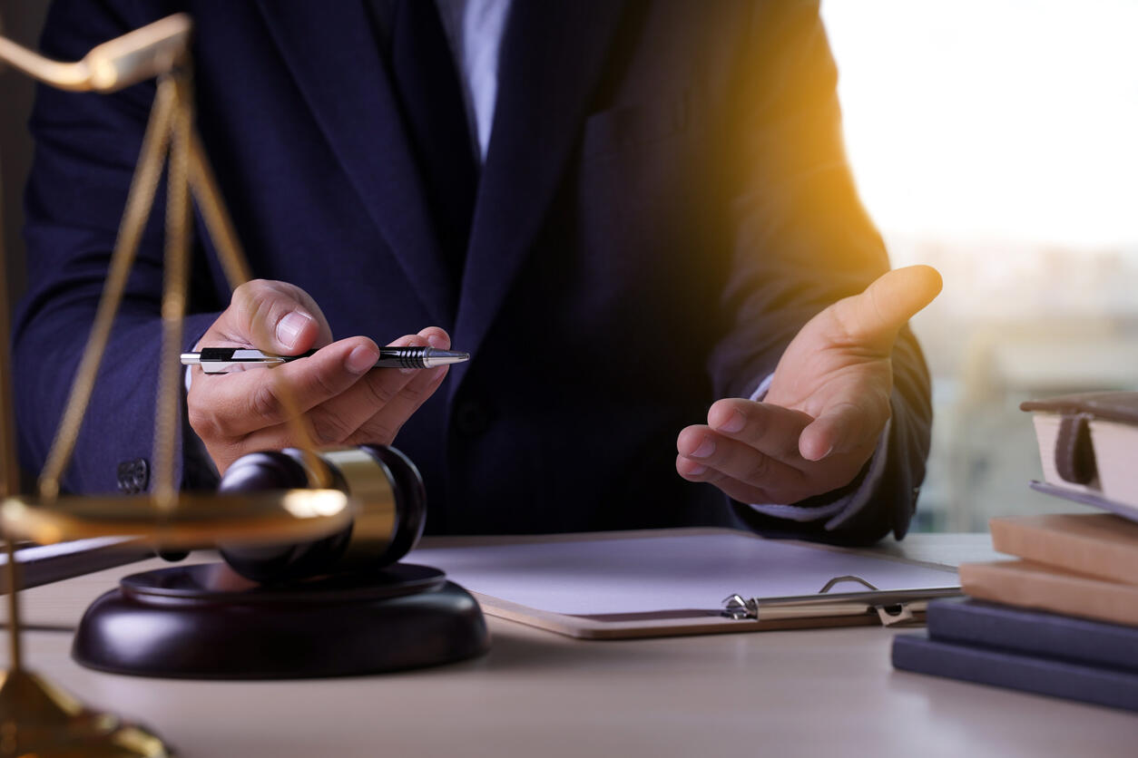 Personal injury attorney gesturing while holding a pen, with scales of justice and a gavel on the desk, symbolizing legal advice and representation in Albany.